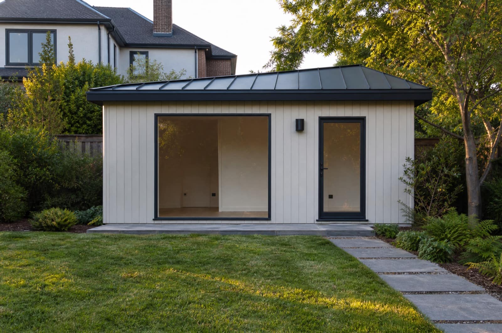 A finished backyard studio at the end of a lawn, the main house behind it